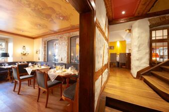 Dining area with wooden chairs and tables set with glasses and napkins in Landhotel Krone featuring decorative ceiling and wall lamps
