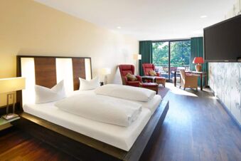 Spacious hotel room at Landhotel Krone with a large bed, two armchairs, a desk, flat-screen TV, and balcony doors with green curtains