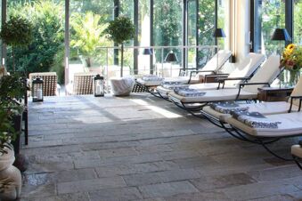 Sunlit relaxation area at Landhotel Krone with stone floor, lounge chairs with cushions, and large glass windows overlooking greenery