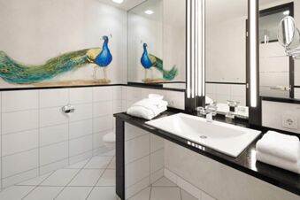 Modern bathroom at Landhotel Krone with white tiles, a black countertop, a large mirror, and a peacock mural on the wall