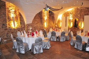 Round tables with white tablecloths and silver-covered chairs set for dining in a stone-walled room at Landhotel Krone