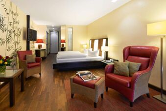 Hotel room at Landhotel Krone with a large bed, two red armchairs, wooden flooring, and soft yellow lighting