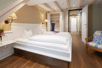 Modern hotel room at Landhotel Krone with wood flooring, white bed, open wardrobe, and patterned chair with cushion