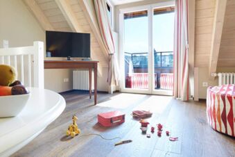 Bright room at Landhotel Krone with wooden floors, a TV on a table, red-striped curtains, and children's toys on the floor