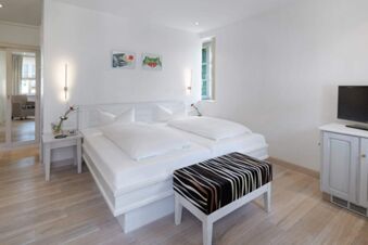 Minimalist bedroom at Landhotel Krone with a white double bed, patterned bench, bedside tables, and wall art
