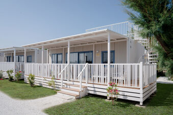White wooden cabins with blue window and door frames, porches, stairs, and spiral staircases surrounded by greenery at Le Mimose Family Resort