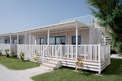 White wooden cabins with blue window and door frames, porches, stairs, and spiral staircases surrounded by greenery at Le Mimose Family Resort