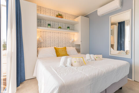 Double bed with white bedding and a yellow pillow under shelves with decorative items and a large mirror at Le Mimose Family Resort