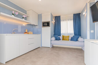 Modern kitchen and seating area with white cabinets, blue walls, microwave, and decorative pillows at Le Mimose Family Resort
