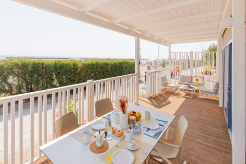 Outdoor covered wooden terrace with dining table set for breakfast and seating area overlooking the beach at Le Mimose Family Resort