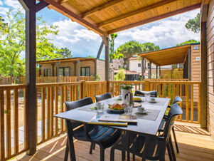 Outdoor covered wooden deck with table, chairs, breakfast items, and surrounding wooden cabins at Le Mimose Family Resort