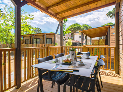 Outdoor covered wooden deck with table, chairs, breakfast items, and surrounding wooden cabins at Le Mimose Family Resort