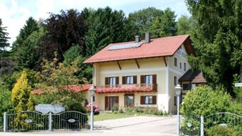 A yellow two-story house with a red tiled roof and flowers on the balcony at Pension Graml Fr&uuml;hst&uuml;ckspension surrounded by trees