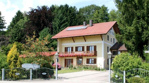 A yellow two-story house with a red tiled roof and flowers on the balcony at Pension Graml Fr&uuml;hst&uuml;ckspension surrounded by trees