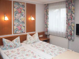 Twin beds with floral bedding and pillows in a room at Pension Graml Fr&uuml;hst&uuml;ckspension with wooden paneling and floral curtains