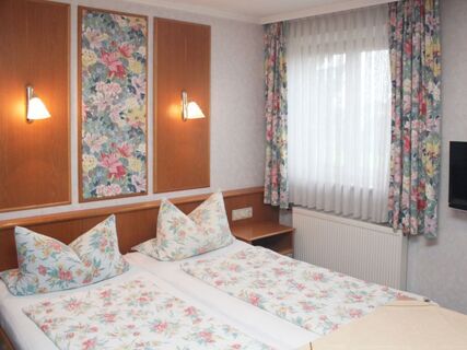 Twin beds with floral bedding and pillows in a room at Pension Graml Fr&uuml;hst&uuml;ckspension with wooden paneling and floral curtains