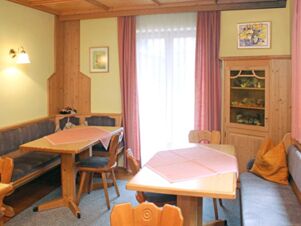 Dining area with wooden tables, chairs, bench seating with cushions, pink tablecloths, curtains, and cabinet at Pension Graml Fr&uuml;hst&uuml;ckspension