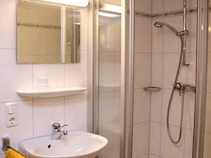 Bathroom in Pension Graml Fr&uuml;hst&uuml;ckspension with white tiles, a sink, mirror, glass shower enclosure, and a handheld showerhead