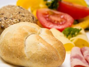 A close-up of a bread roll, multigrain bread, sliced tomato, cheese, parsley, and rolled ham from Pension Graml Fr&uuml;hst&uuml;ckspension breakfast plate