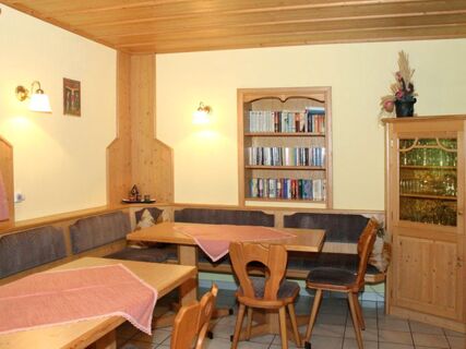 Dining area with wooden tables and chairs, built-in bench seating, a bookshelf, and a glass-front cabinet at Pension Graml Fr&uuml;hst&uuml;ckspension