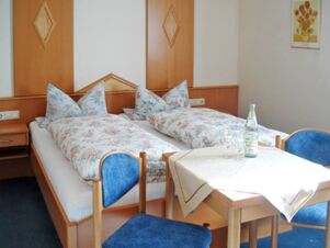 A twin bedroom at Pension Graml Fr&uuml;hst&uuml;ckspension with floral bedding, wooden furniture, blue chairs, and a table with a bottle and glasses