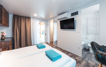 Bedroom at Tenuta Primero Grado Family Resort with two beds, turquoise towels, wall-mounted TV, air conditioner, and open bathroom door