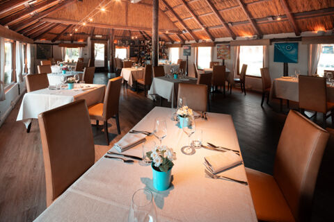 Dining area with tables covered in white cloths and brown chairs under a wooden thatched roof at Tenuta Primero Grado Family Resort