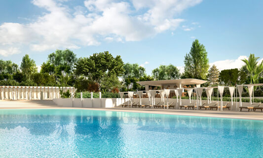 Large blue swimming pool with white cabanas and lounge chairs surrounded by lush green trees at Tenuta Primero Grado Family Resort