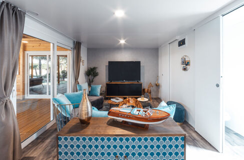 Living room with blue and gray furniture, wooden floor, model boat on table, TV, and sliding doors at Tenuta Primero Grado Family Resort