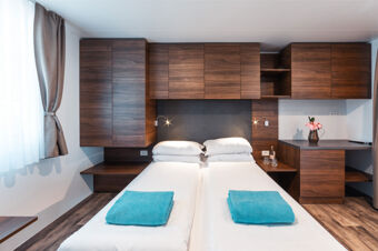 Double bed with white linens and turquoise towels in a wooden cabin room with windows and shelves at Tenuta Primero Grado Family Resort