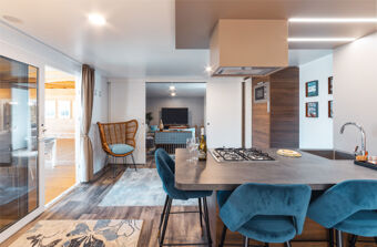 Open kitchen with gas stove, blue velvet chairs, rattan chair, sliding doors, and living area seen in Tenuta Primero Grado Family Resort