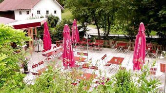 Outdoor seating area with red umbrellas and wooden tables at Hotel Restaurant Pension Weiherm&uuml;hle surrounded by greenery