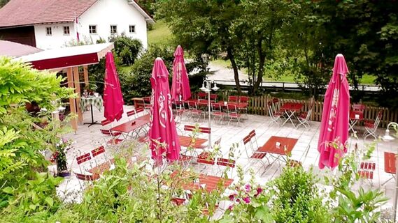 Outdoor seating area with red umbrellas and wooden tables at Hotel Restaurant Pension Weiherm&uuml;hle surrounded by greenery