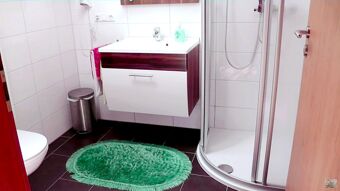 Bathroom with a white sink cabinet, green oval rug, silver trash can, and curved shower in Hotel Restaurant Pension Weiherm&uuml;hle