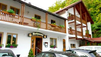 Facade of Hotel Restaurant Pension Weiherm&uuml;hle with wooden balconies, flower pots, entrance door, and several parked cars in front