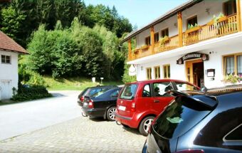 Cars parked on a cobblestone parking lot in front of the Hotel Restaurant Pension Weiherm&uuml;hle building surrounded by trees