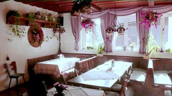 Hele ja hubane restoran Hotel Restaurant Pension Weiherm&uuml;hle puidust m&ouml;&ouml;bli, laudlinade ja suurtel akendel rippuvate taimedega.