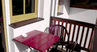 A small outdoor balcony area with a red table, two black chairs, one gray chair, and an ashtray at Hotel Restaurant Pension Weiherm&uuml;hle
