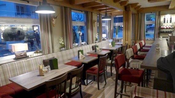 Gem&uuml;tlicher Restaurantbereich im Hotel R&ouml;ssle mit Holzm&ouml;beln, karierten Sitzb&auml;nken, roten St&uuml;hlen und dekorativen Details am Fenster.