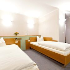 Two single beds with white bedding and wooden frames in a bright room at Hotel Hahnen with wall lights and a small flower vase