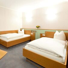 Two single beds with white bedding and pillows in a simple, clean room at Hotel Hahnen with wooden furniture and soft lighting