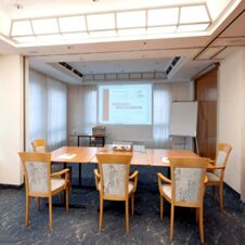 Moderne og lyst seminarrom i Hotel Hahnen med stoler, bord, projektor og velkomstskjerm for m&oslash;ter.