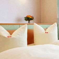 Two white pillows on a bed with a wooden headboard and a small bouquet of flowers behind it at Hotel Hahnen