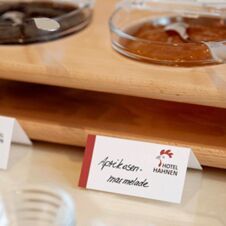 N&aelig;rbilde av et lite kort med p&aring;skriften aprikossyltet&oslash;y p&aring; frokostbuffeen p&aring; Hotel Hahnen, omgitt av sm&aring; sk&aring;ler med syltet&oslash;y.