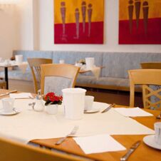 Table set for breakfast with cups, cutlery, a small red flower plant, and napkins in Hotel Hahnen dining area