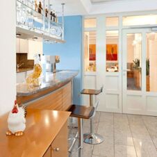 Bar area with two black bar stools, glassware hanging above, and a ceramic rooster at Hotel Hahnen