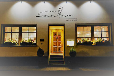 Restaurant Saalbau entrance with illuminated windows, potted plants, and wall signage at Winzerhotel Weingut Kinges-Kessel