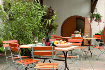 Outdoor seating area with orange wooden chairs and tables with wine bottles, glasses, fruit, and greenery at Winzerhotel Weingut Kinges-Kessel