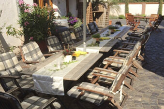 Outdoor dining area at Winzerhotel Weingut Kinges-Kessel with wooden tables, cushioned chairs, potted plants, and stone flooring