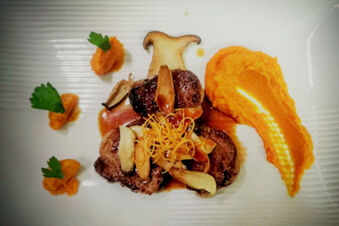 A gourmet dish with grilled meat, mushroom slices, orange puree, and garnishes served on a white plate at Winzerhotel Weingut Kinges-Kessel